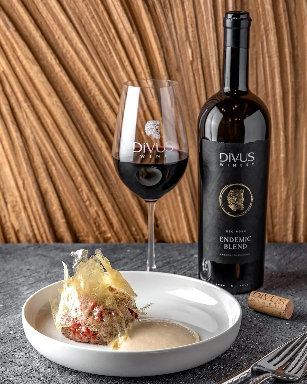 O sticlă Divus și un pahar de vin roșu lângă un desert